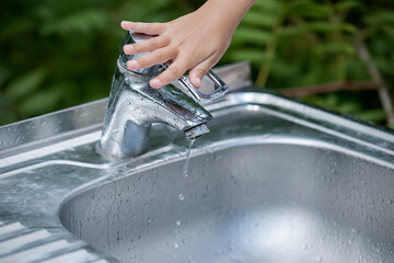 Baby try to turn off water faucet but water still leak. A child's hand turning off the tap. Save...