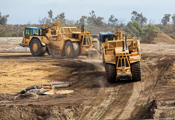 Heavy earthmoving equipment including scapers and motor graders involved in grading operations at a construction site