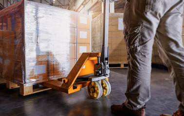 Warehouse worker working with hand pallet jack unloading cargo boxes at the warehouse storage....