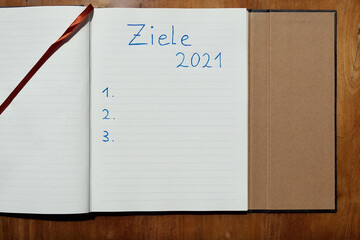 Die Festlegung von Zielen für das Jahr 2021 auf einem linierten Papier auf einer Holzunterlage mit...