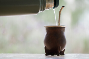 Selective focus shot of a thermos pouring water in  calabash mate cup with straw - yerba mate tea...