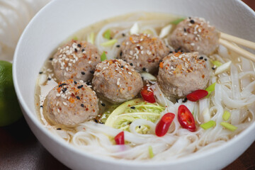 Closeup of a white bowl with pork meatballs, cabbage and pho noodles in a broth, selective focus