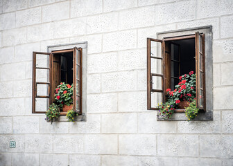 Fototapeta na wymiar Wooden windows with flowers in the old sandstone house
