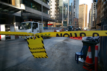 Safety workplace yellow striped caution tape warning sign barricade exclusion zone preventing from public access while construction road worker working on street Sydney city CBD, Australia        