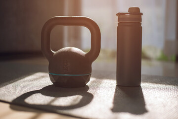 gym equipment, kettlebell dumbbell weight and bottle of water on yoga mat at home.