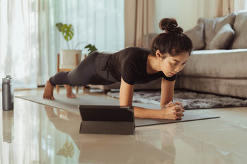 Fit woman doing yoga plank and watching online yoga class. young woman exercising at home.