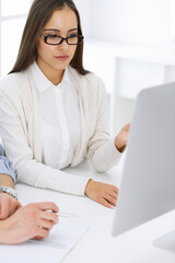 Young woman sitting at the desk with computer in white colored office. Looks like student girl or business lady communicating with casual dressed man