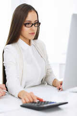 Young business woman and man sitting and working with computer and calculator in office. Bookkeeper checking balance or making finance report. Tax and audit concepts