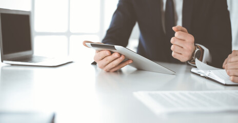 Unknown business people using tablet computer in modern office. Businessman or male entrepreneur is working with his colleague at the desk