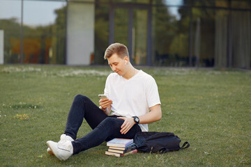 Student in a park. Boy in a university campus . Man sitting on a grass with a books.