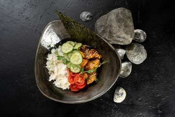Teriyaki chicken with rice and vegetables. A hot main course with chicken fillet, boiled rice, cucumbers and tomatoes, garnished with sesame seeds, nori and young sprouts of green peas.