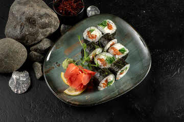Sushi rolls with salmon and chuka salad. A traditional Japanese dish of raw fish fillets, cream cheese, boiled rice, chuka salad and nori with ginger, wasabi, lemon and young shoots of green peas.