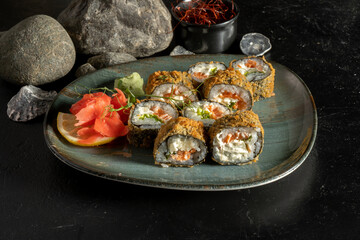 Sushi rolls baked in batter with salmon and salad. A traditional Japanese dish of raw fish fillets, cream cheese, boiled rice, lettuce and nori with ginger, wasabi, lemon and young sprouts of peas.