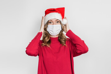 Fototapeta na wymiar Caucasian shocked surprised young woman in santa hat and red sweater holding her head isolated on white studio background