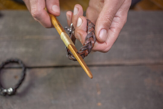 Bracelet leather handicraft. Pigtail accessory. Man s hands making handicraft leather on beautiful old wood background. Polishing tool handmade.