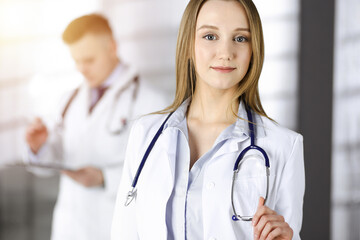 Professional beautiful woman-doctor with a stethoscope is standing straight in a sunny clinic. Young doctors at work in a hospital. Perfect medicine concept
