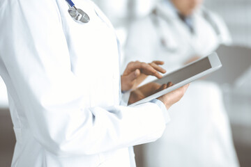 Unknown woman doctor is checking some data at computer tablet, close up. Young doctors at work in a hospital. Medicine and healthcare concept