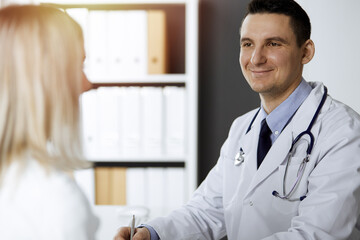 Friendly male doctor and patient woman discussing current health examination while sitting in sunny...