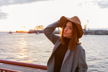 Fototapeta premium Stylish woman in felt hat and coat at sunrise at sea