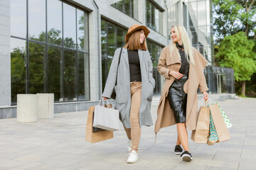 Two women shopaholic friend in autumn clothes are holding many shopping bags and walking around the city. Lifestyle, leisure concept