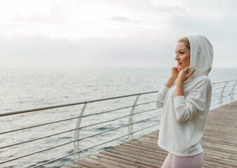 Portrait of attractive cute sportswoman in white hoodie on the beach