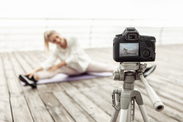 Fitness blogging. Young healthy sports woman recording workout on camera with tripod and showing how to do exercise on the beach. Vlogging