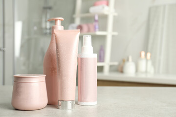 Set of hair care cosmetic products covered with water drops on light grey stone table in bathroom. Space for text