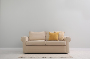 Fototapeta na wymiar Comfortable beige sofa near light wall indoors, space for text. Simple interior