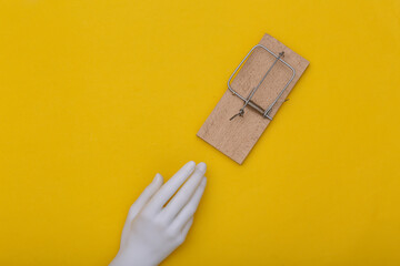 The mannequin's hand reaches for a mousetrap on yellow background. Trap concept. Top view