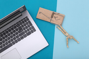 Puppet caught in a mousetrap and laptop on a blue background. Online trap
