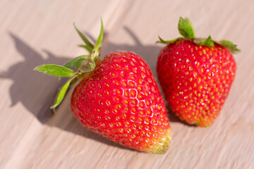 Macro photo of two ripe strawberries on wooden background. Long shadows because of hard summer sunlight.