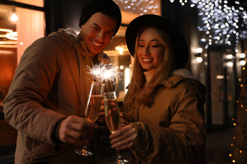Happy couple with sparklers and glasses of champagne at winter fair