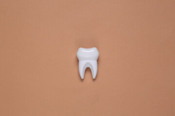Fake tooth and white hand on brown background. Top view