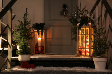 Decorative lanterns and small Christmas trees near house entrance