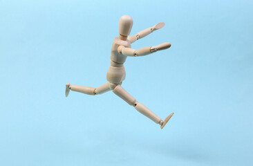 Cheerful wooden puppet jumping on blue background