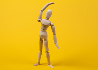 Wooden puppet practicing aerobics on yellow background. Healthy lifestyle