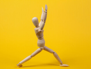 Wooden puppet practicing yoga asana pose on yellow background