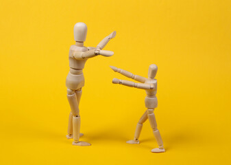 Wooden puppets hug on a yellow background. Parental love concept