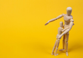 Wooden puppets hug on a yellow background. Parental love concept