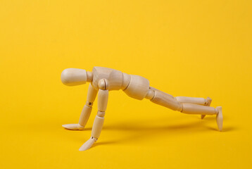 Wooden puppet push ups on yellow background. Sport concept