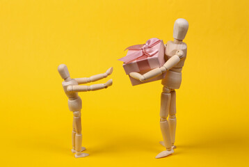 Wooden puppet presents gift box to child on yellow background