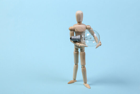 Wooden puppet holding light bulb on a blue background.
