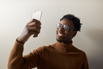 Cute cheerful young Afro American male holding cell phone using front camera for video conference...