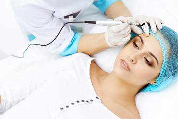 Naklejka premium Professional beautician doing eyebrow tattoo at woman face. Permanent brow makeup in beauty salon, closeup. Cosmetology treatment