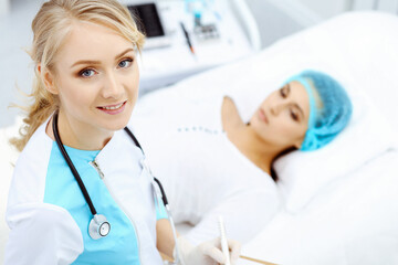 Female doctor and young woman patient in hospital. Physicians examine girl lying at the bed, view from above