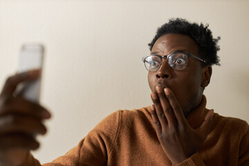 Oh my God. Astonished fearful young Afro American male covering mouth in shock, lost for words,...