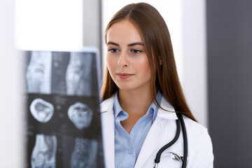 Doctor woman examining x-ray picture while standing near window in hospital. Surgeon or orthopedist...