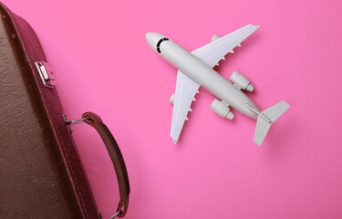 Travel concept. Old luggage and airplane figurine on pink background. Flight voyage, trip, journey. Flat lay composition. Top view