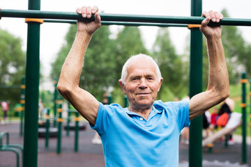 Naklejka premium mature cheerful pensioner man doing physical exercises on sports equipped playground