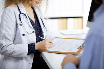 Female doctor and male patient discussing current health examination while sitting in clinic,...